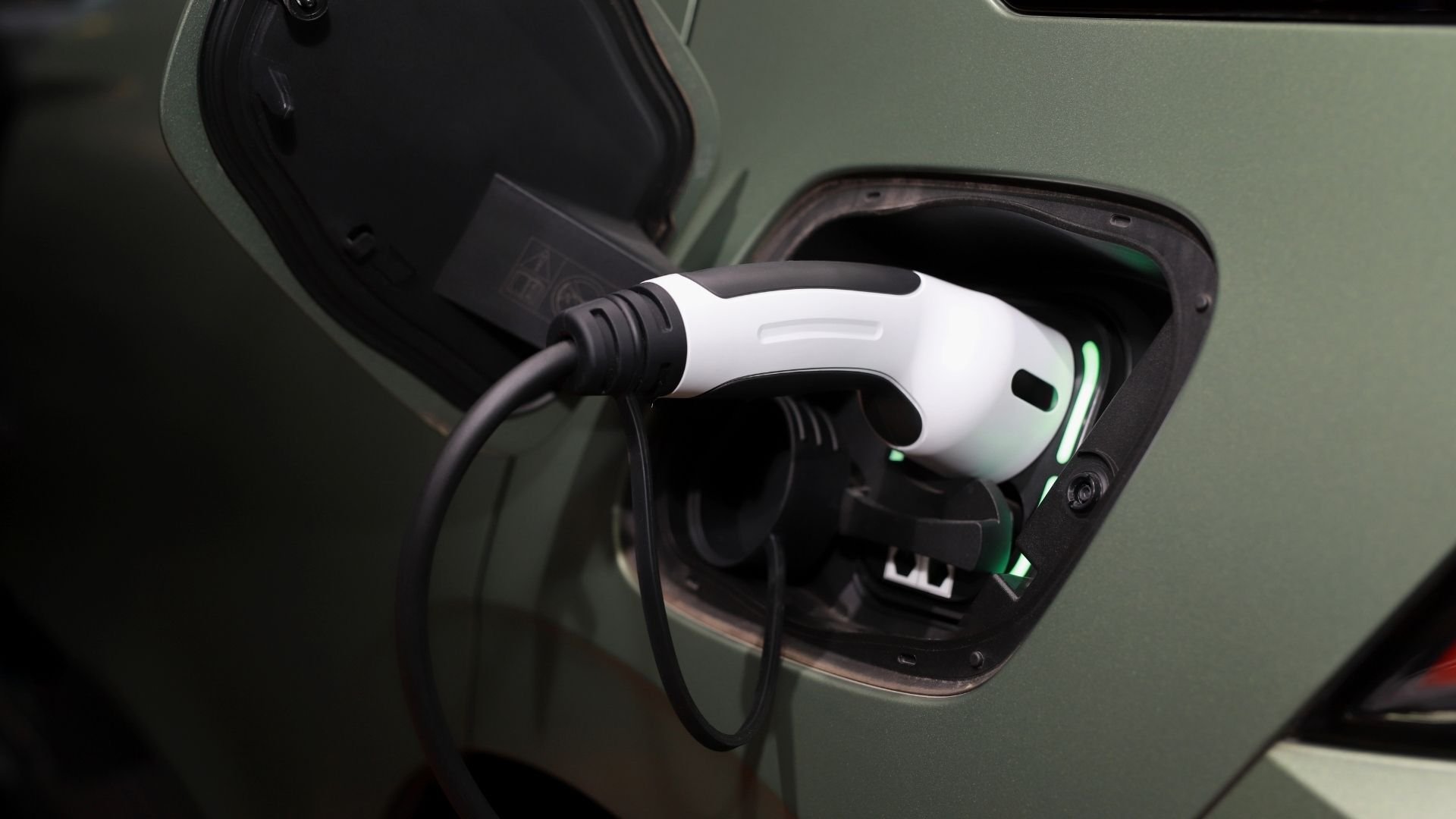 White and black electric car charging cable plugged into green vehicle port