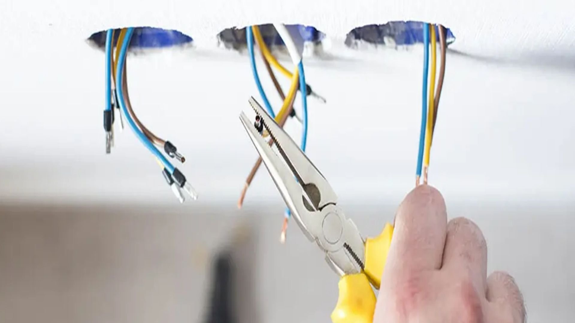 Electrical cables hanging with colorful wires and metal connectors, held by pink gloved hand.