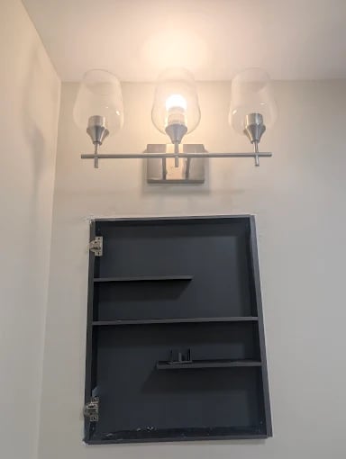 Three-light bathroom vanity fixture above black wall cabinet on white wall