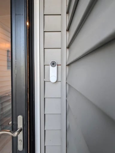 White smart doorbell mounted on modern white door frame with digital lock visible