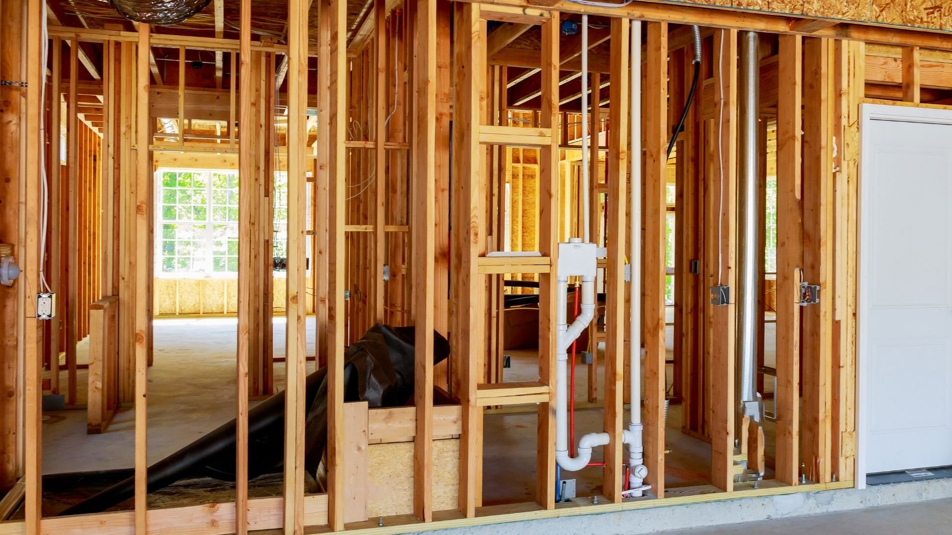 Interior wood framing of house under construction with pipes and wiring visible