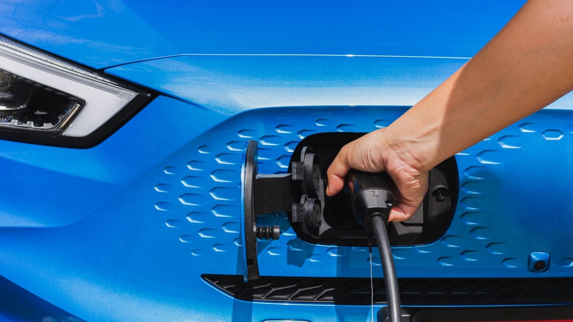 Hand plugging charging cable into blue electric vehicle charging port